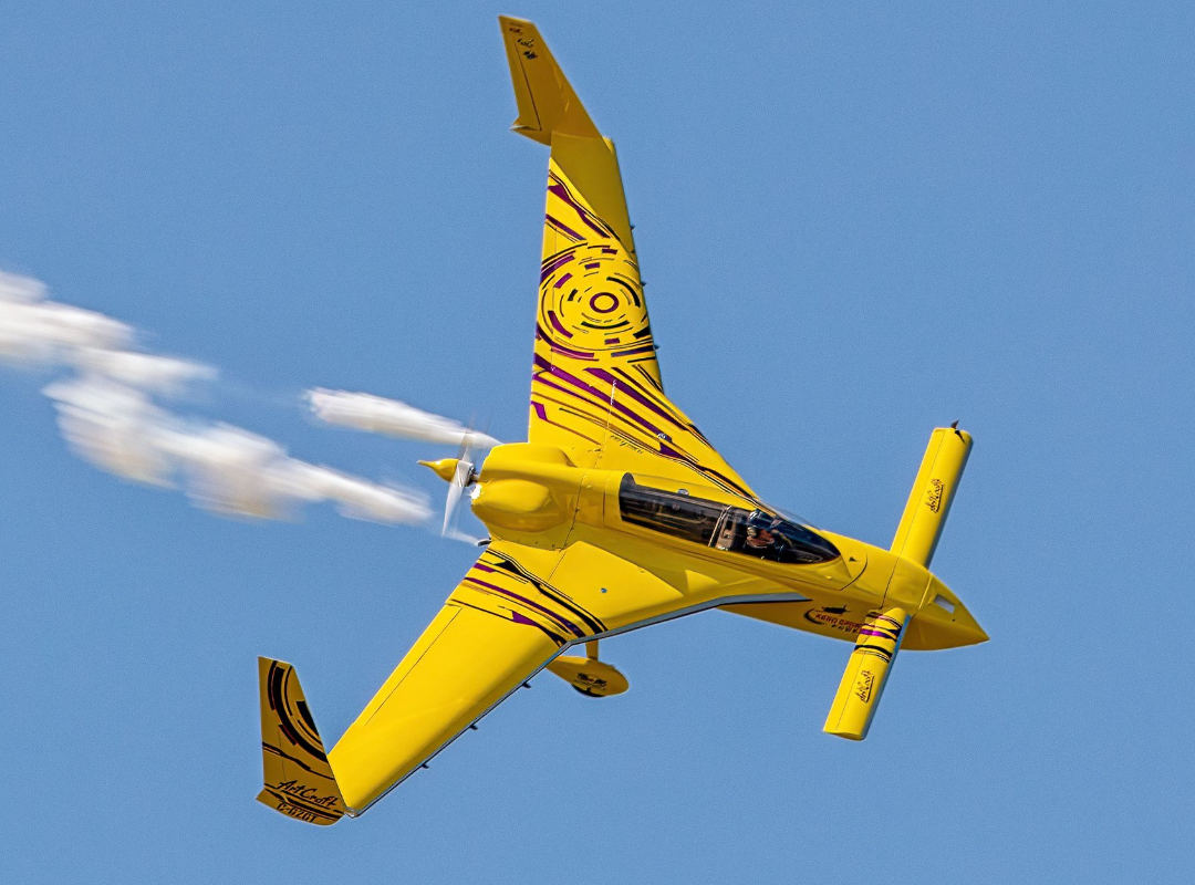 Kyle Fowler in his bright yellow with purple graphics Long EZ flying against a clear blue sky.