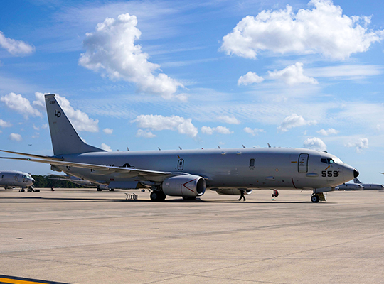 U.S. Navy P-8 Poseidon aircraft parked on tarmac under a blue sky with scattered clouds