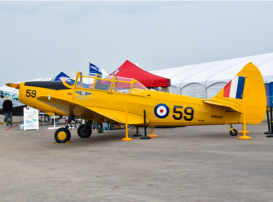 Yellow PT-26 training aircraft on display with RAF roundels and event tents behind it