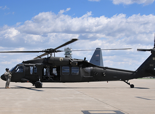 U.S. Army UH-60 Black Hawk helicopter parked on tarmac with crew member standing nearby