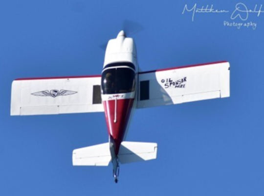 Brett Hunter of Waynesville, Ohio performs in a small aerobatic aircraft, viewed from below against a clear blue sky during flight.