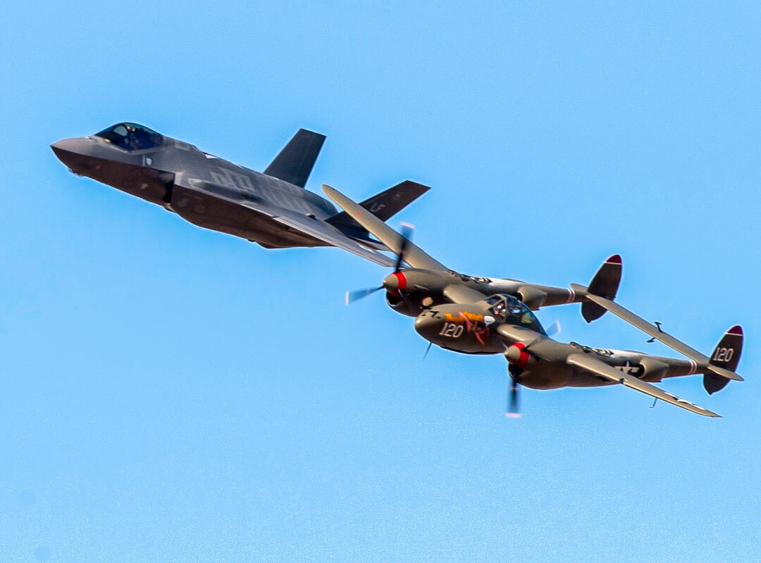 U.S. Air Force F-35A Lightning II and a vintage P-38 Lightning fly together in a Heritage Flight demonstration against a clear blue sky.